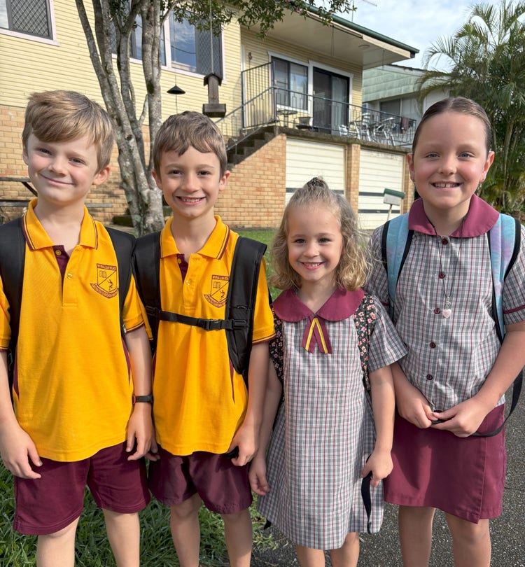 A photo of 4 students in school uniform standing at the school gate and smiling