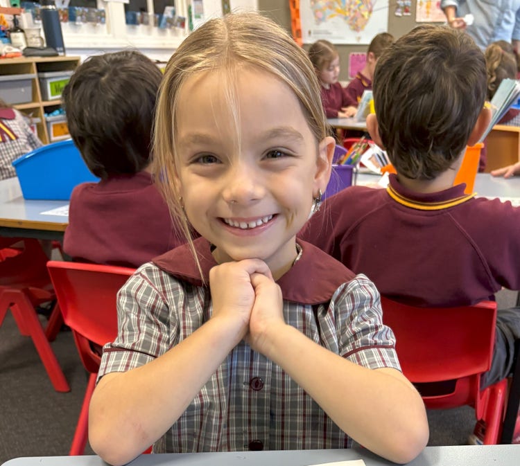 An image of a student sitting at a desk smiling at the camera