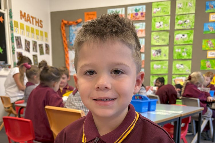 A young boy in a classroom smiling at the camera