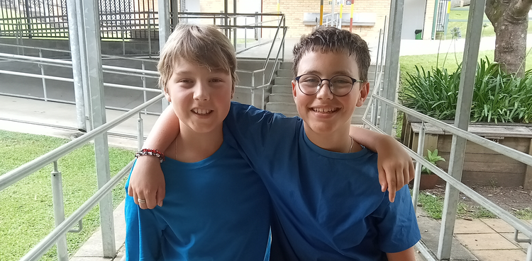 Two students standing with their arms around each other and wearing blue shirts